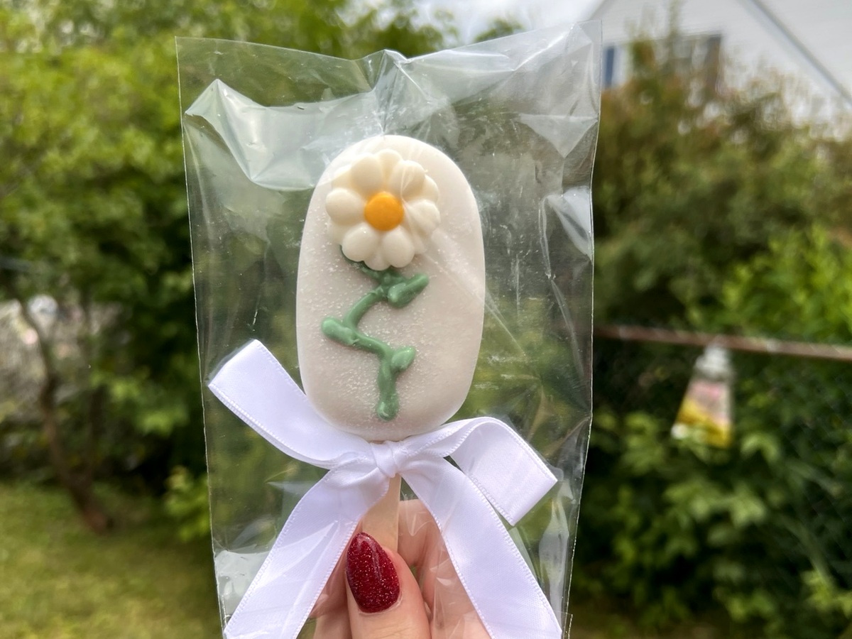 White daisy cakesicle held in hand with ribbon bow